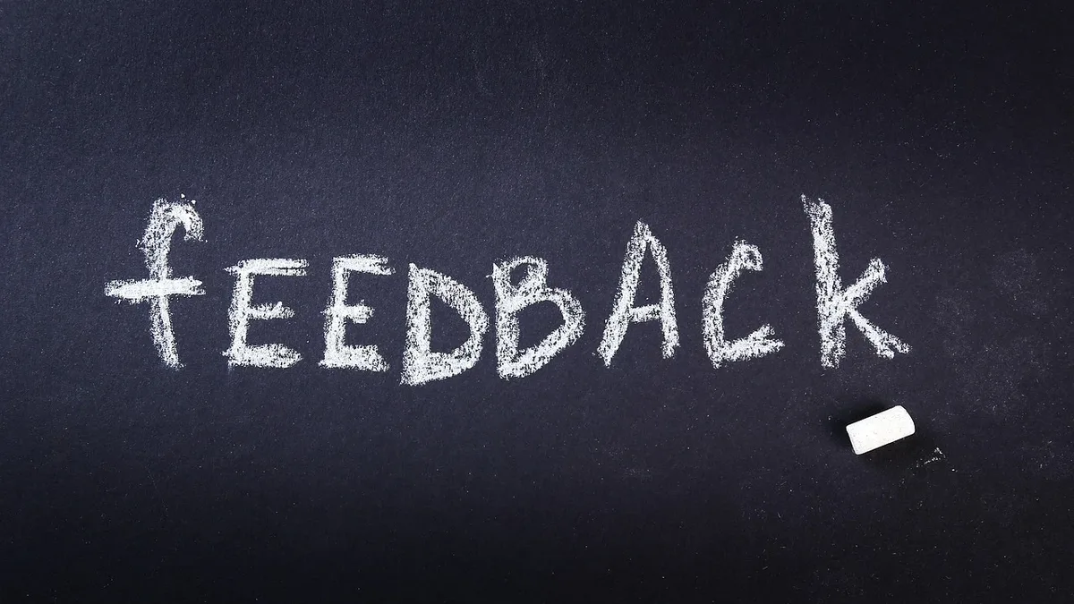 A blackboard with the word "feedback" written in white chalk, accompanied by a piece of white chalk lying on the board.