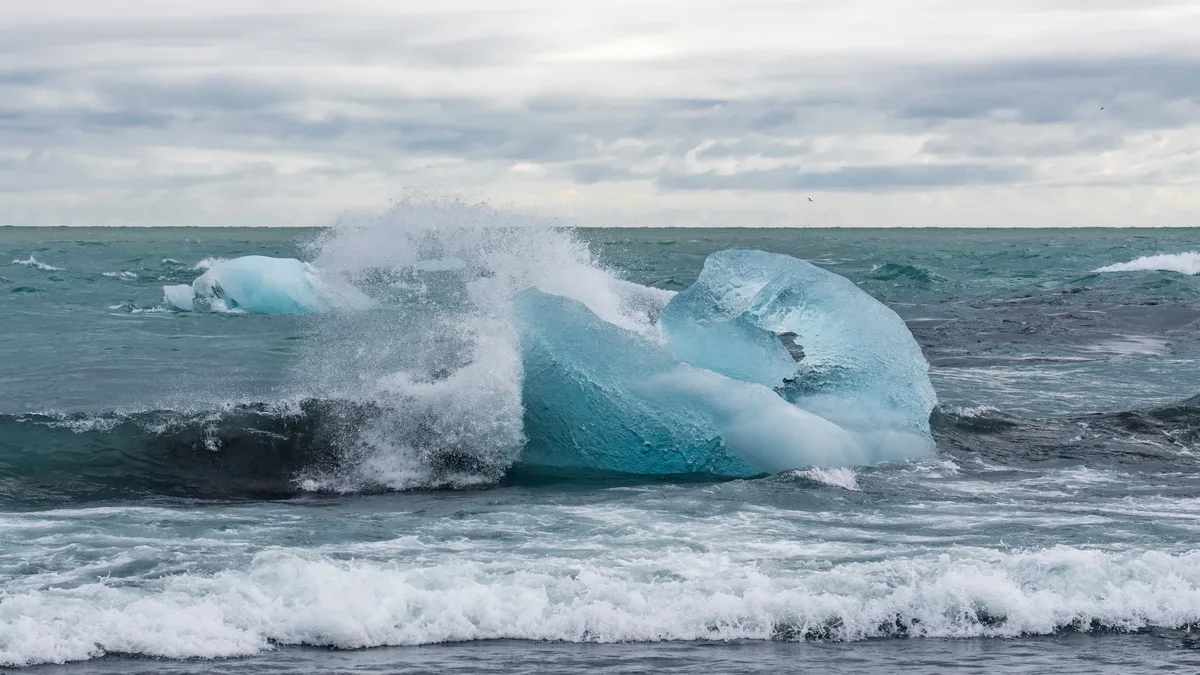 A large piece of ice, likely from a glacier, being propelled by waves in the ocean.
